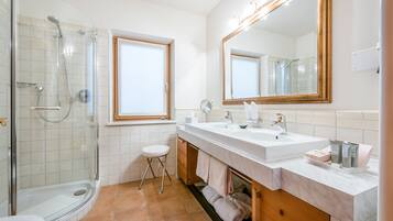 Ein modernes Badezimmer mit einer begehbaren Glasdusche, zwei Waschbecken, einem großen Spiegel und einem Fenster.