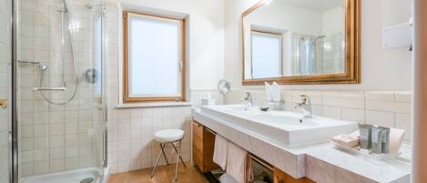 Un baño moderno con ducha envuelta en vidrio, dos lavamanos, un espejo grande y una ventana.