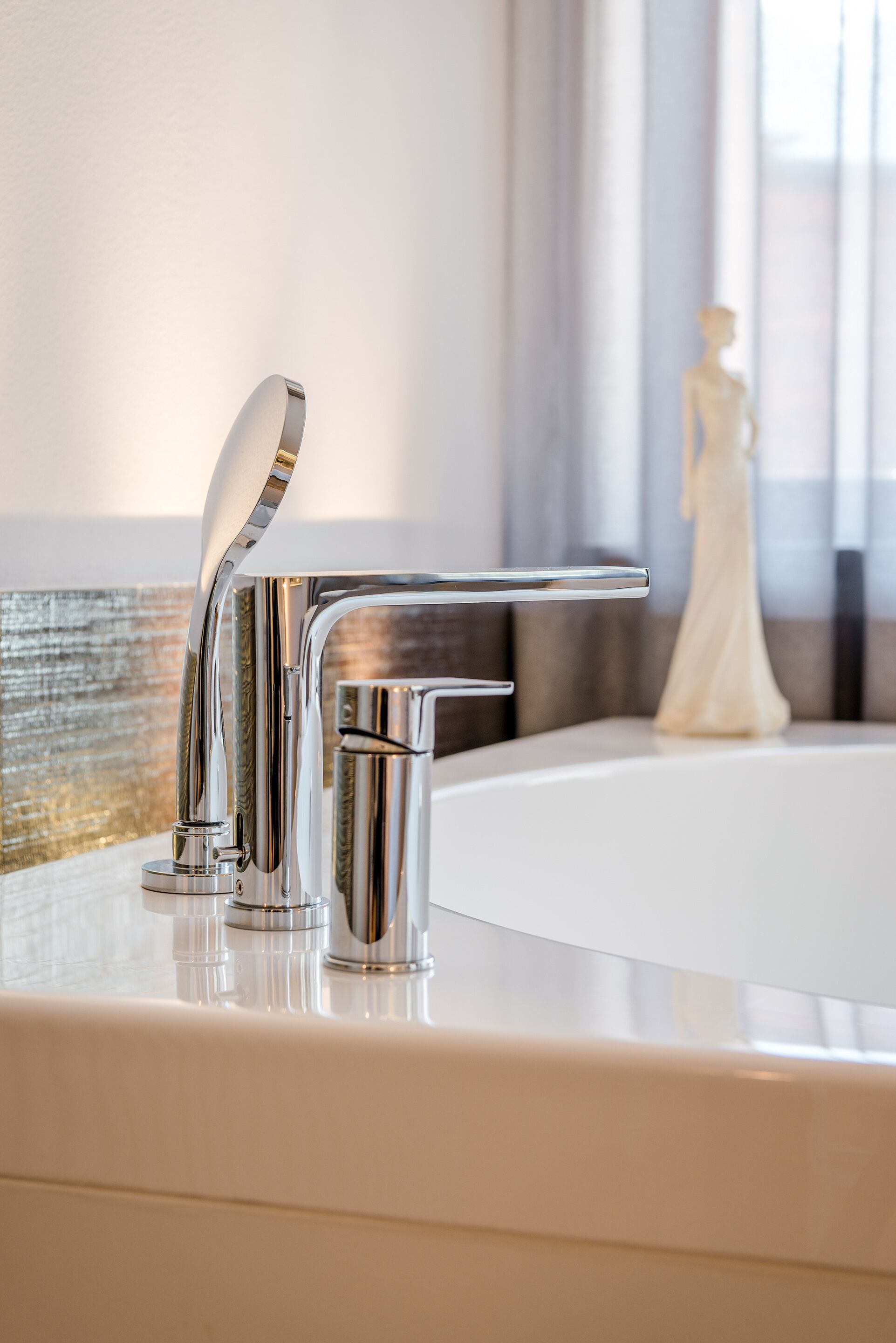 A modern bathroom with a chrome faucet, a bathtub, and a decorative vase.