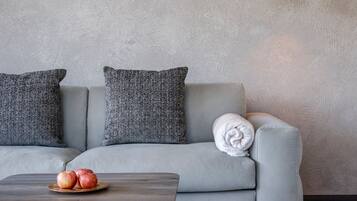 Una sala de estar moderna con un sofá gris, dos almohadas grises, una mesa redonda con manzanas y una lámpara colgante dorada.