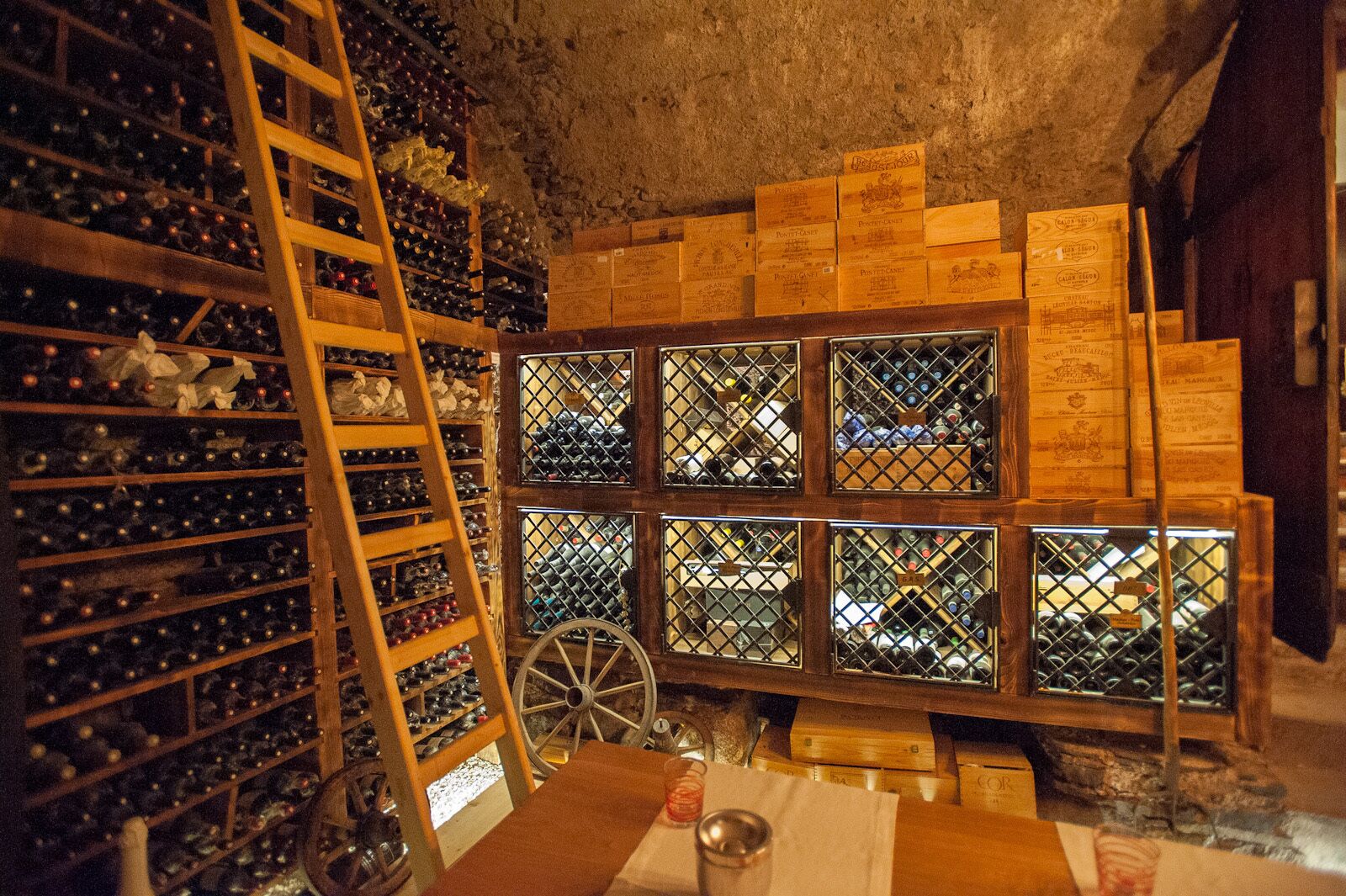 Une cave à vin avec des étagères en bois et une roue, ainsi que des caisses en bois empilées contre le mur.