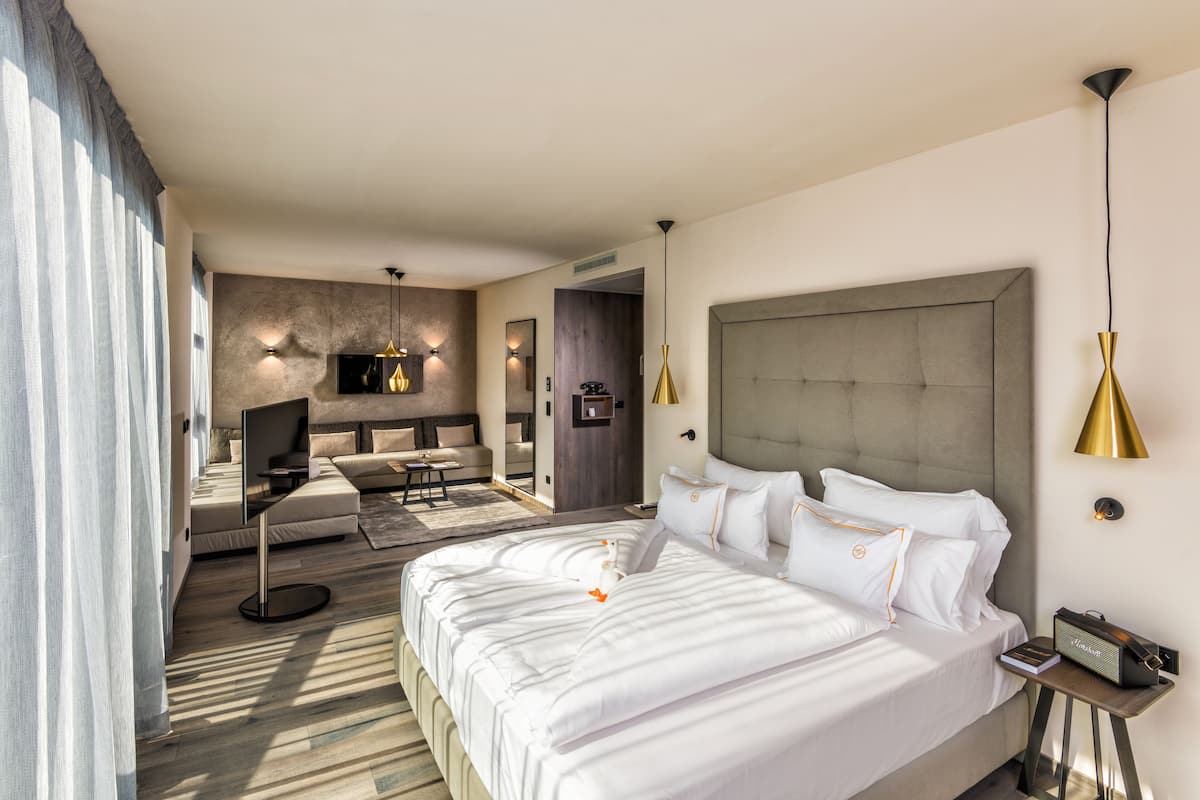 A modern hotel room with a large bed, a sofa, a TV, and a desk.