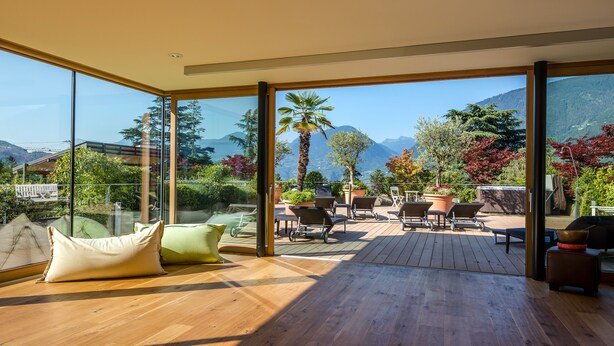 Ein geräumiger Balkon mit Holzboden, großen Glasfenstertüren und Blick auf Berge und Bäume.