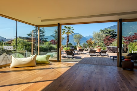 A spacious balcony with a wooden floor, large glass doors, and a view of mountains and trees.