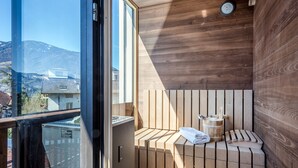 Eine moderne Sauna mit Holzlamellen, einem Handtuch und einem Holzeimer, mit Blick auf Berge durch ein großes Fenster.