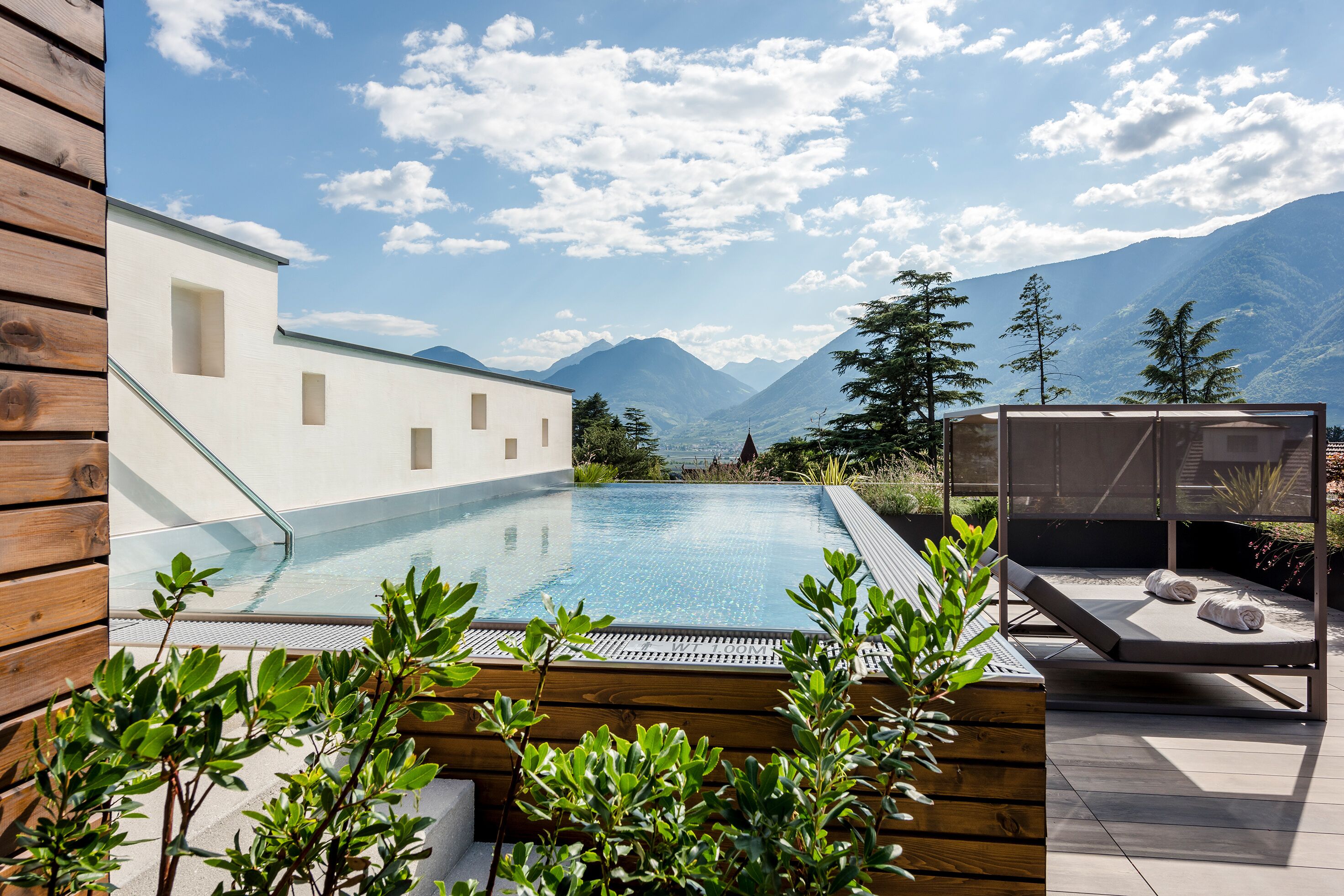 Zona de piscina con vistas a las montañas, terraza de madera y una silla de descanso.