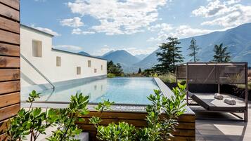 Zona de piscina con vistas a las montañas, terraza de madera y una silla de descanso.