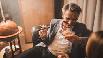 Un uomo seduto su una poltrona in pelle, con un sigaro e un bicchiere di whisky.