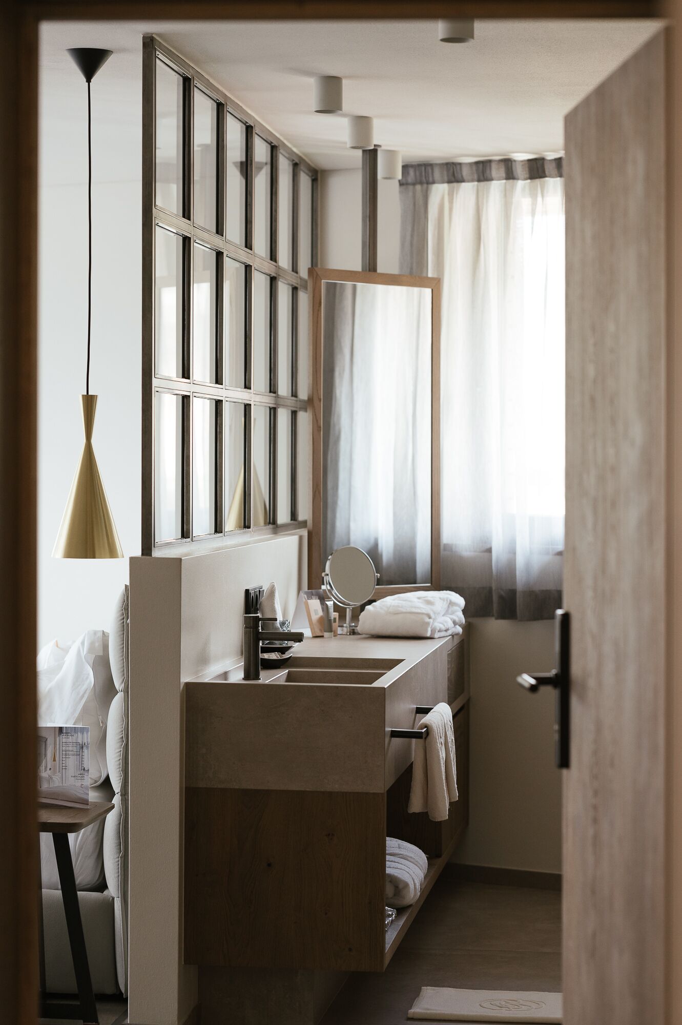 Un baño pequeño con tocador de madera, un espejo grande y una ventana con cortinas.