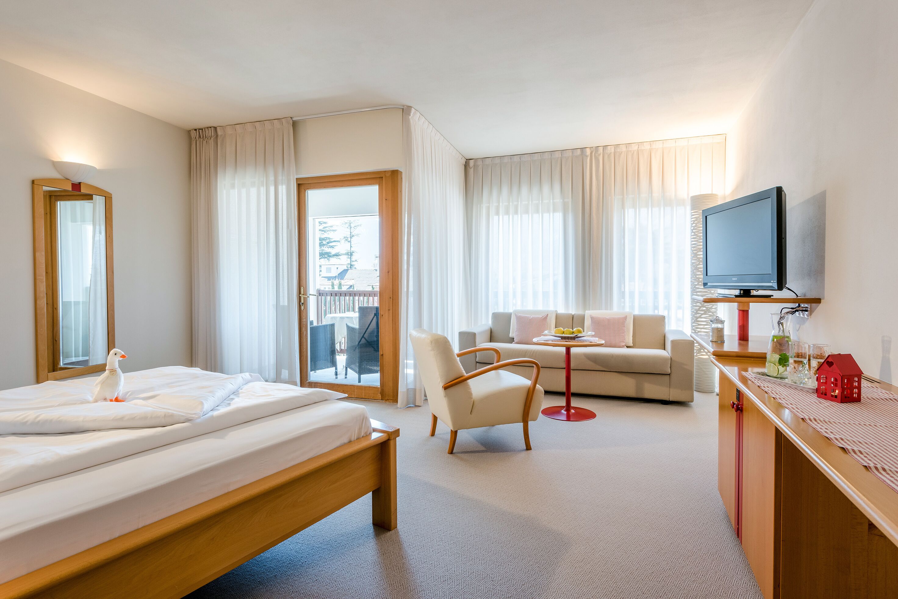 Une chambre d’hôtel avec un lit, une chaise, un canapé, une télévision et un balcon avec des rideaux.