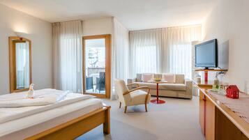 A hotel room with a bed, a chair, a sofa, a TV, and a balcony with curtains.