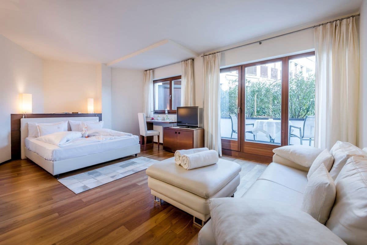 A modern hotel room with a bed, a sofa, a TV, and a desk.