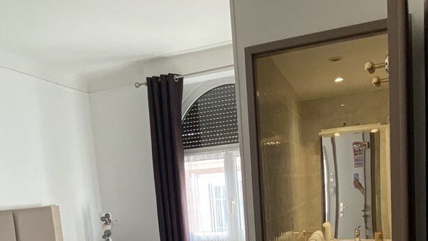 A hotel room with two beds, a bathroom with a mirror, and a view of the outside. - Hotel Lutetia (Cannes)