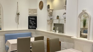 A restaurant interior with white walls, a chalkboard menu, and a blue booth. Tables are set with white tablecloths and chairs. - Hotel Lutetia (Cannes)
