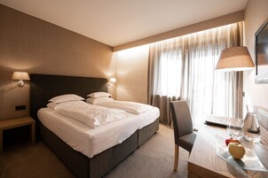 Habitación de hotel con una cama grande, lámparas de noche, un escritorio con silla y una ventana con cortinas.