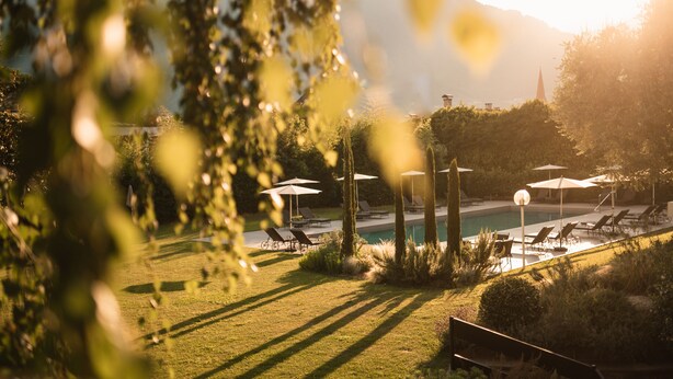 Un área de piscina con sillas de descanso y sombrillas, rodeada de vegetación y una montaña al fondo.