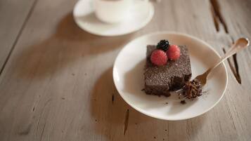 Una porción de pastel de chocolate con frutos rojos sobre un plato blanco, una cuchara y una taza de café en un platillo al fondo.