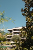 Un hotel moderno de varios pisos con piscina, mobiliario exterior y vistas a la montaña.