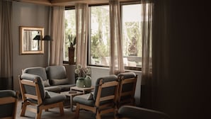 Una sala de estar acogedora con un sofá, dos sillones, una mesita con adornos y una ventana con cortinas.