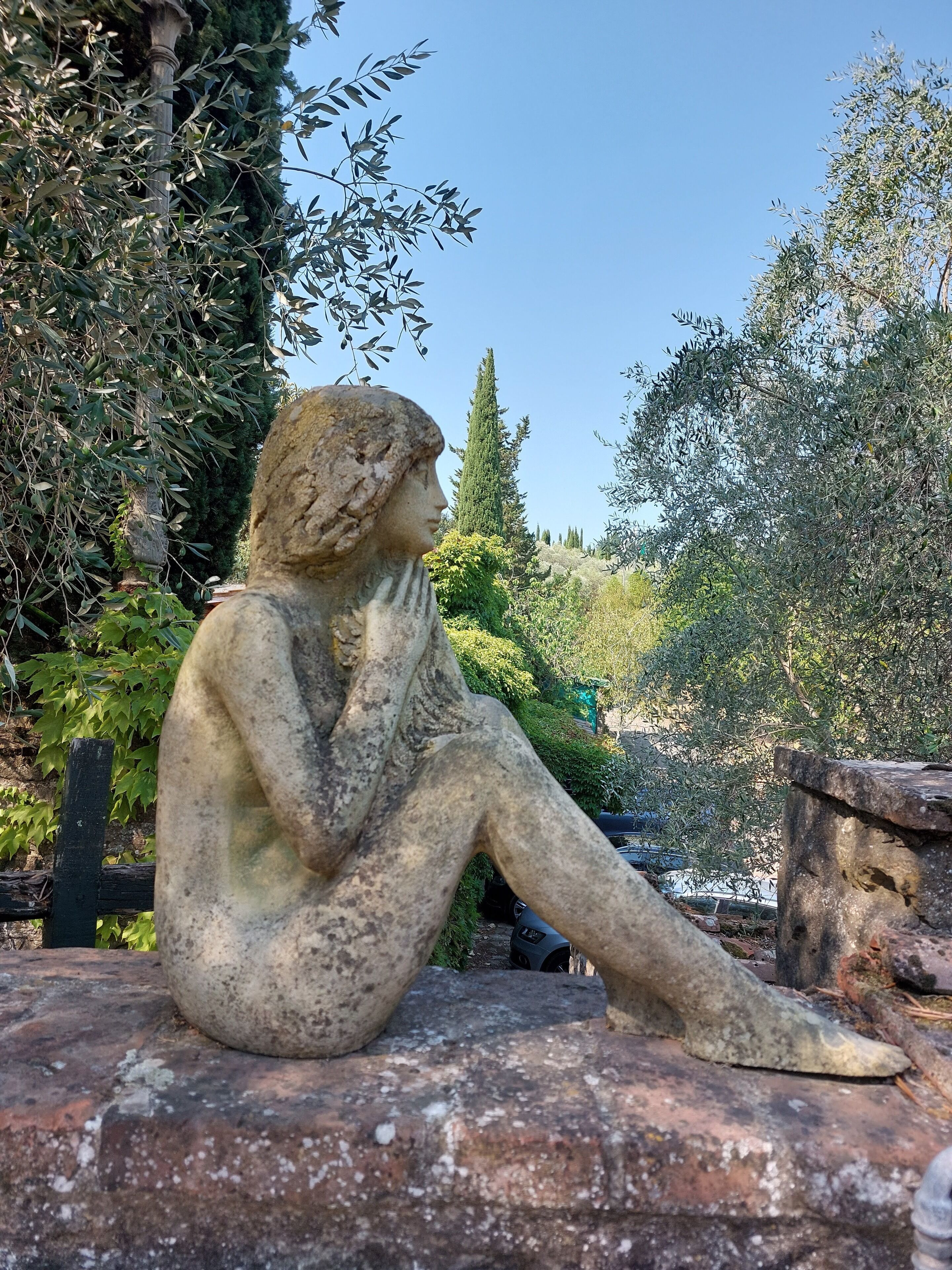 A stone statue of a seated figure in a garden setting.