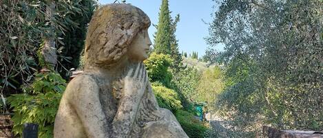 A stone statue of a seated figure in a garden setting.