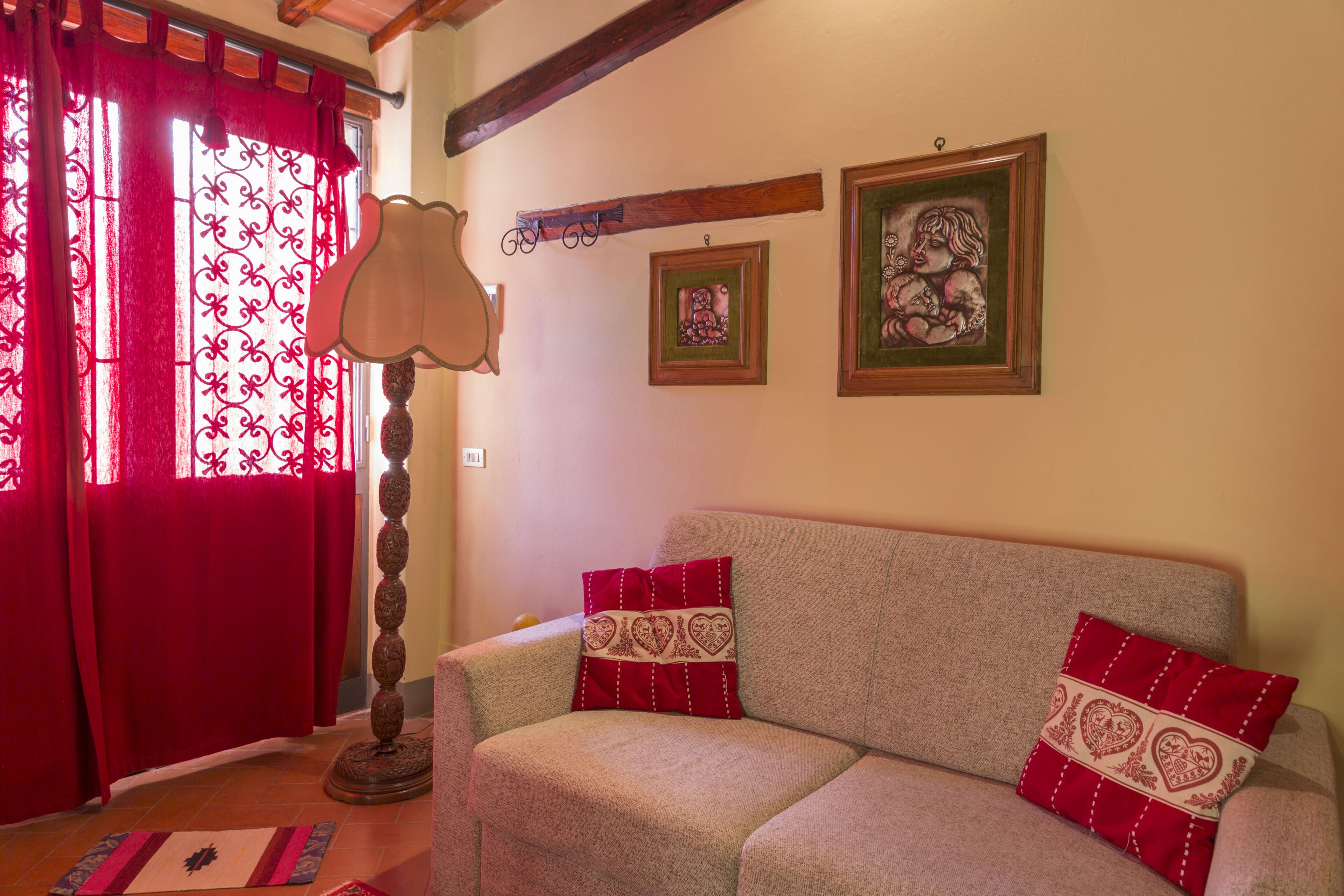 Uma sala de estar com um sofá, almofadas vermelhas, um abajur e duas molduras na parede.