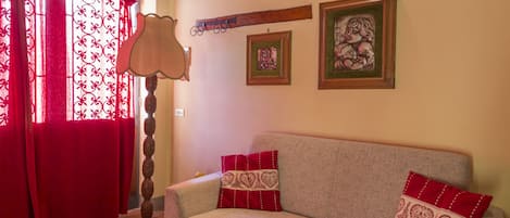A living room with a sofa, red cushions, a floor lamp, and two framed pictures on the wall.