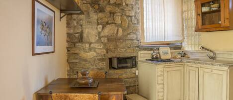 A kitchen with a stone wall, wooden cabinets, a microwave, and a dining area with a table and chairs.