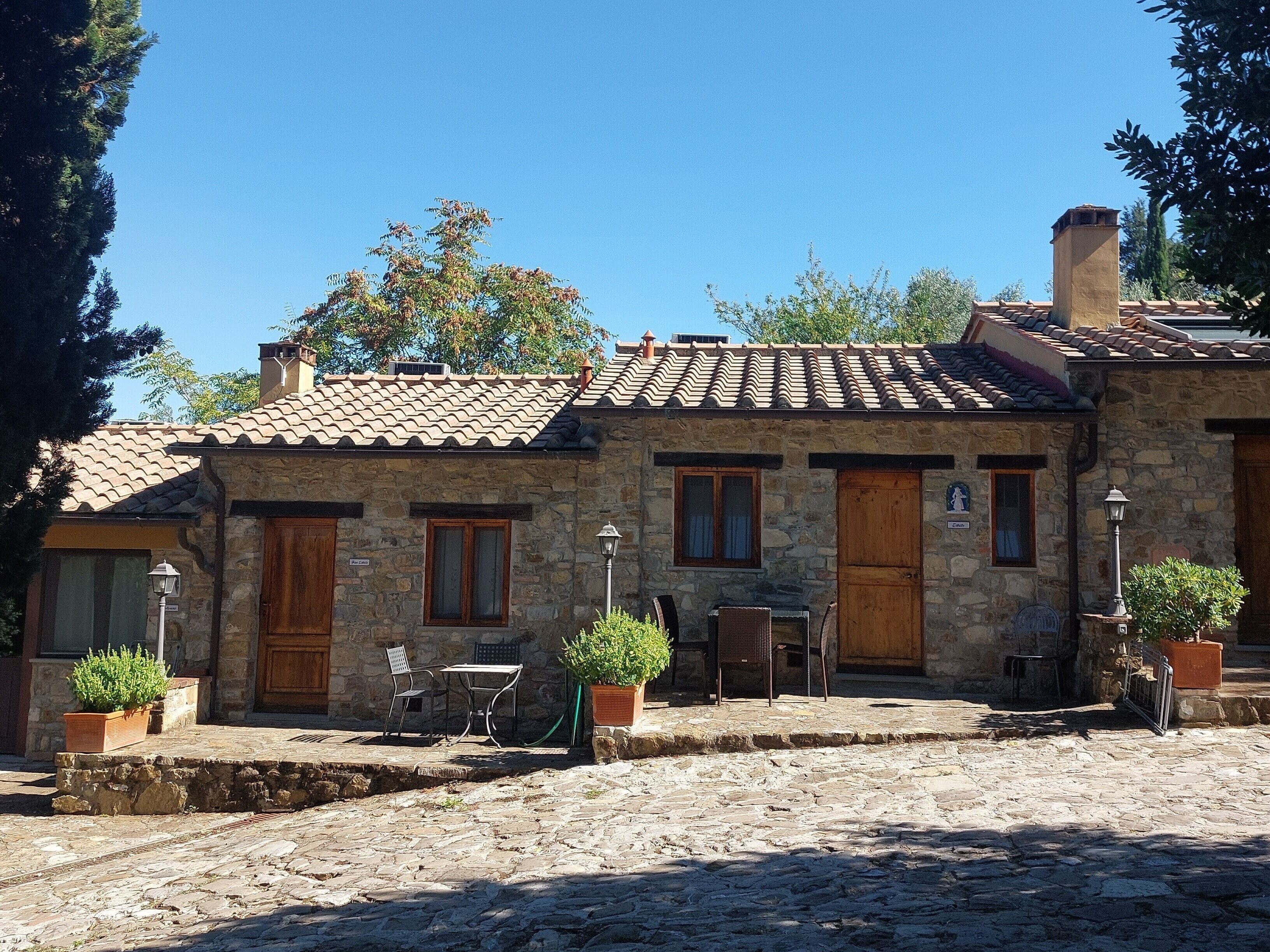 A stone building with a tiled roof, two wooden doors, and a small outdoor seating area with a table and chairs.