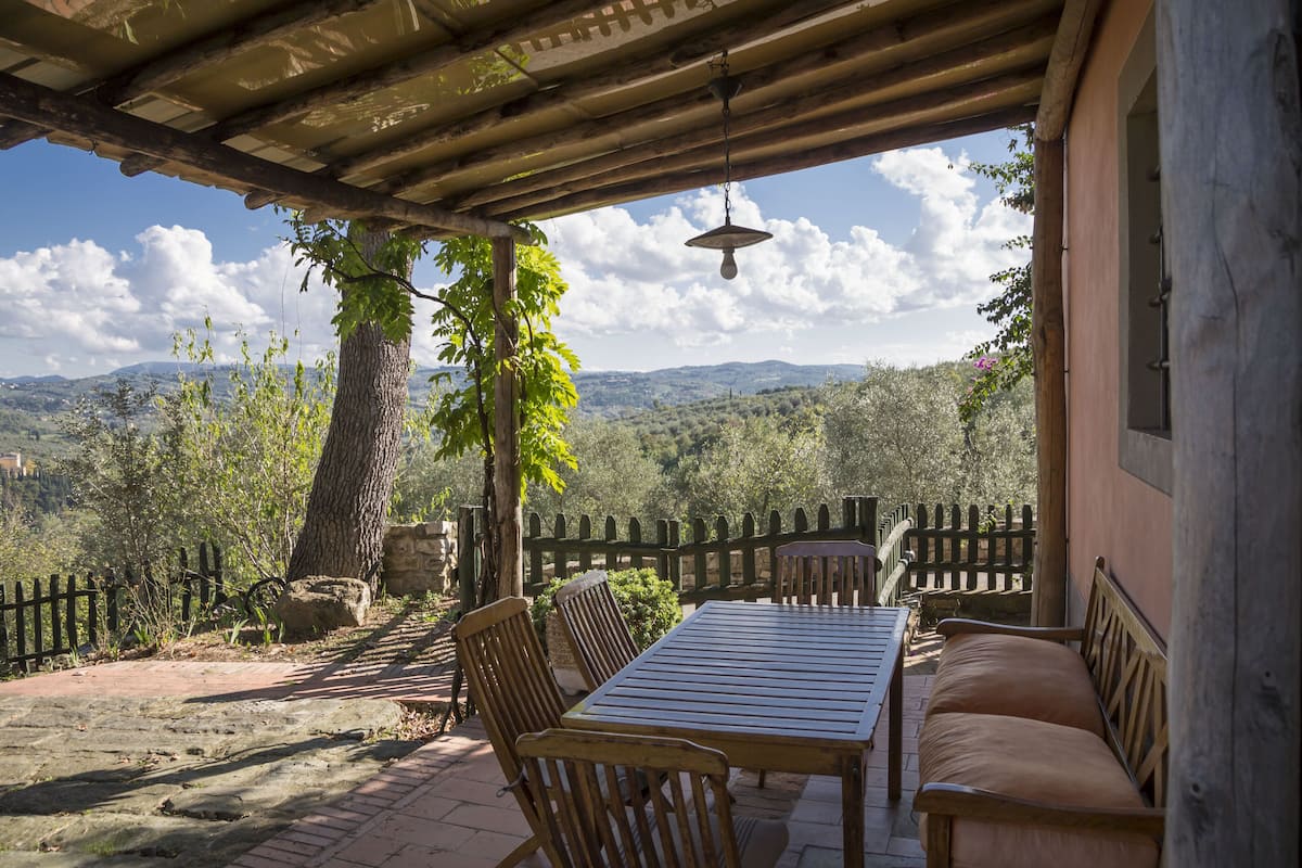 Eine überdachte Terrasse mit Tisch und Stühlen, einer Hängelampe und Blick ins Grüne.