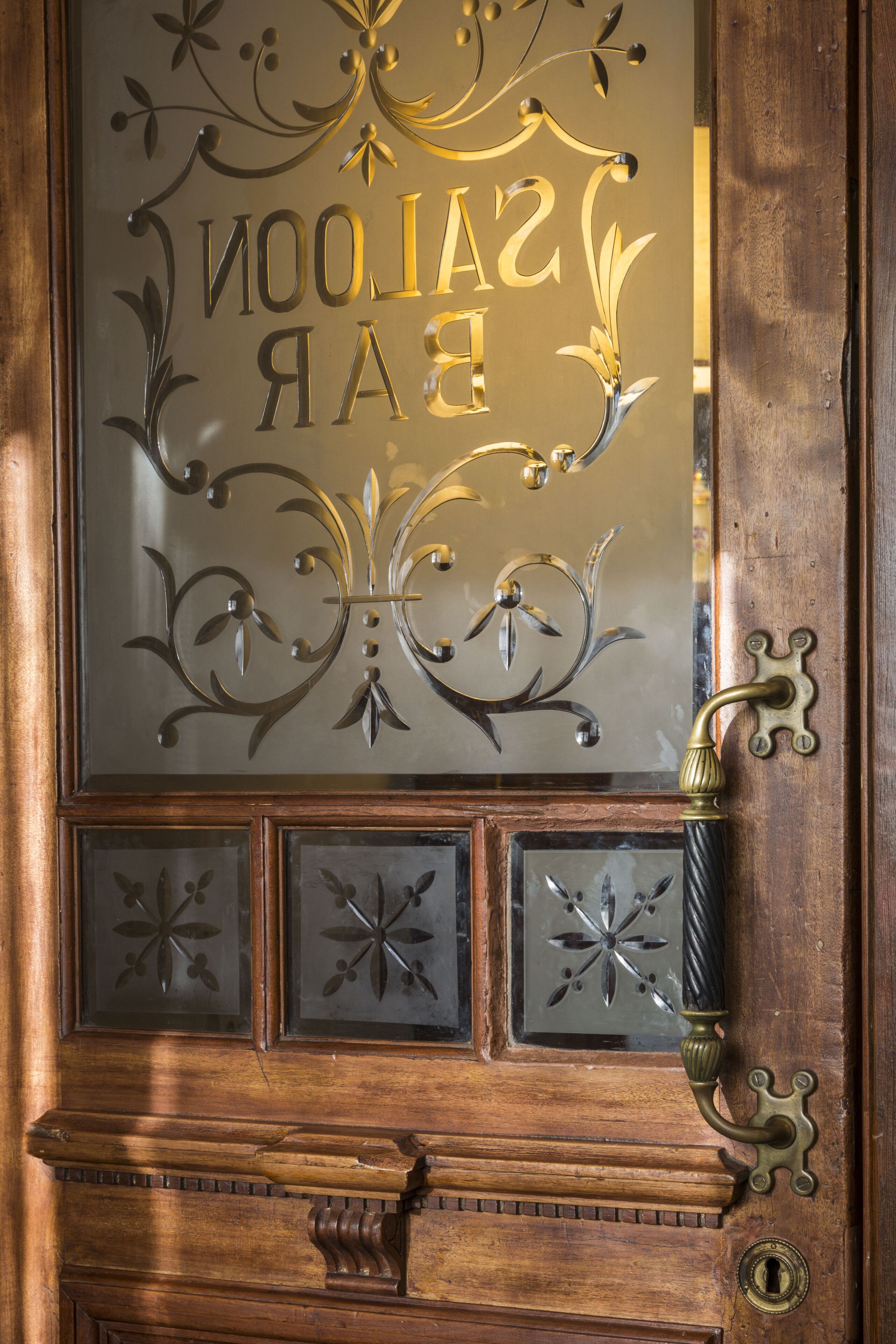 A wooden door with a glass panel featuring decorative metalwork and the text "SAINTS BAR."