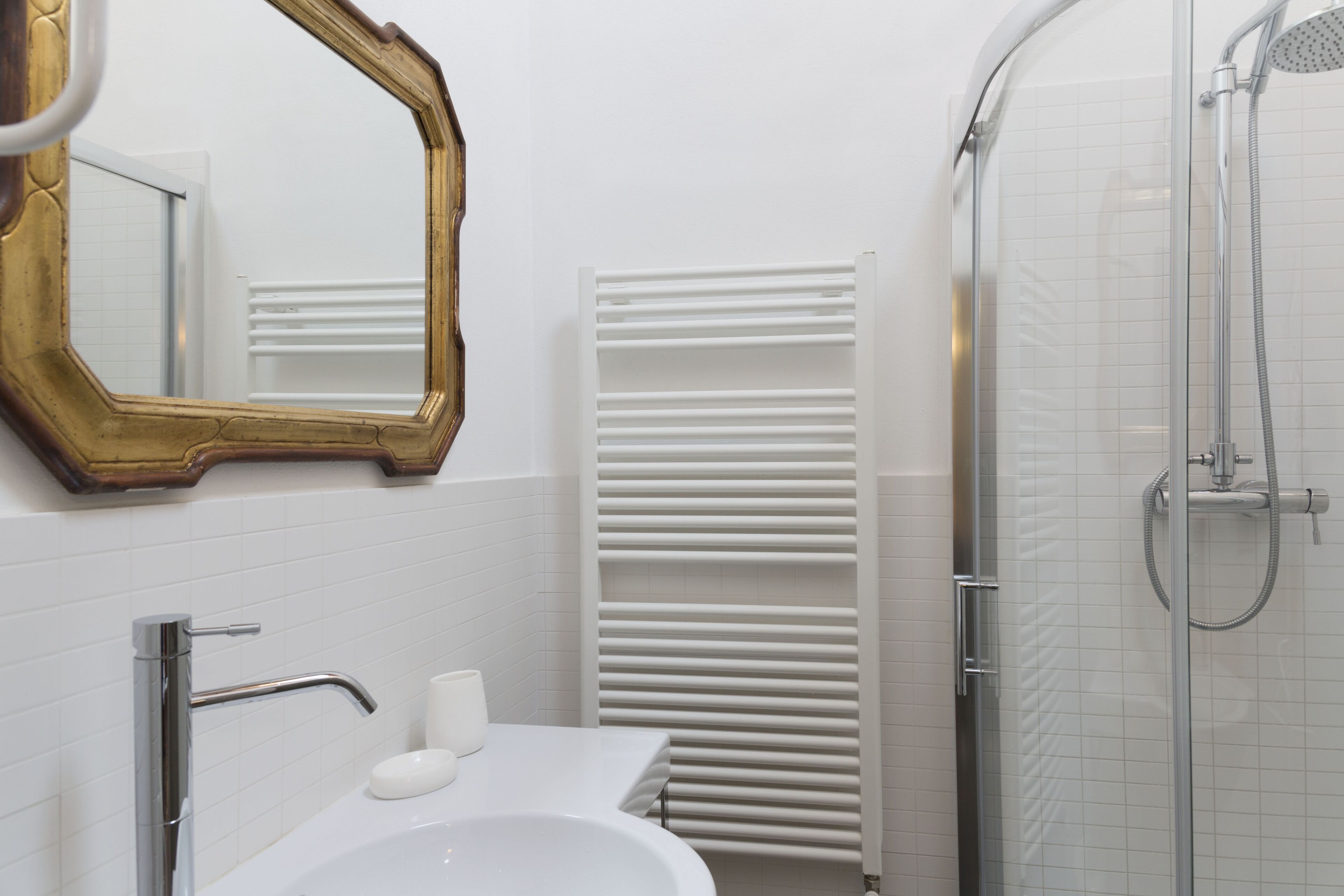 A bathroom with a white sink, a mirror with a gold frame, a towel rack, and a shower area.