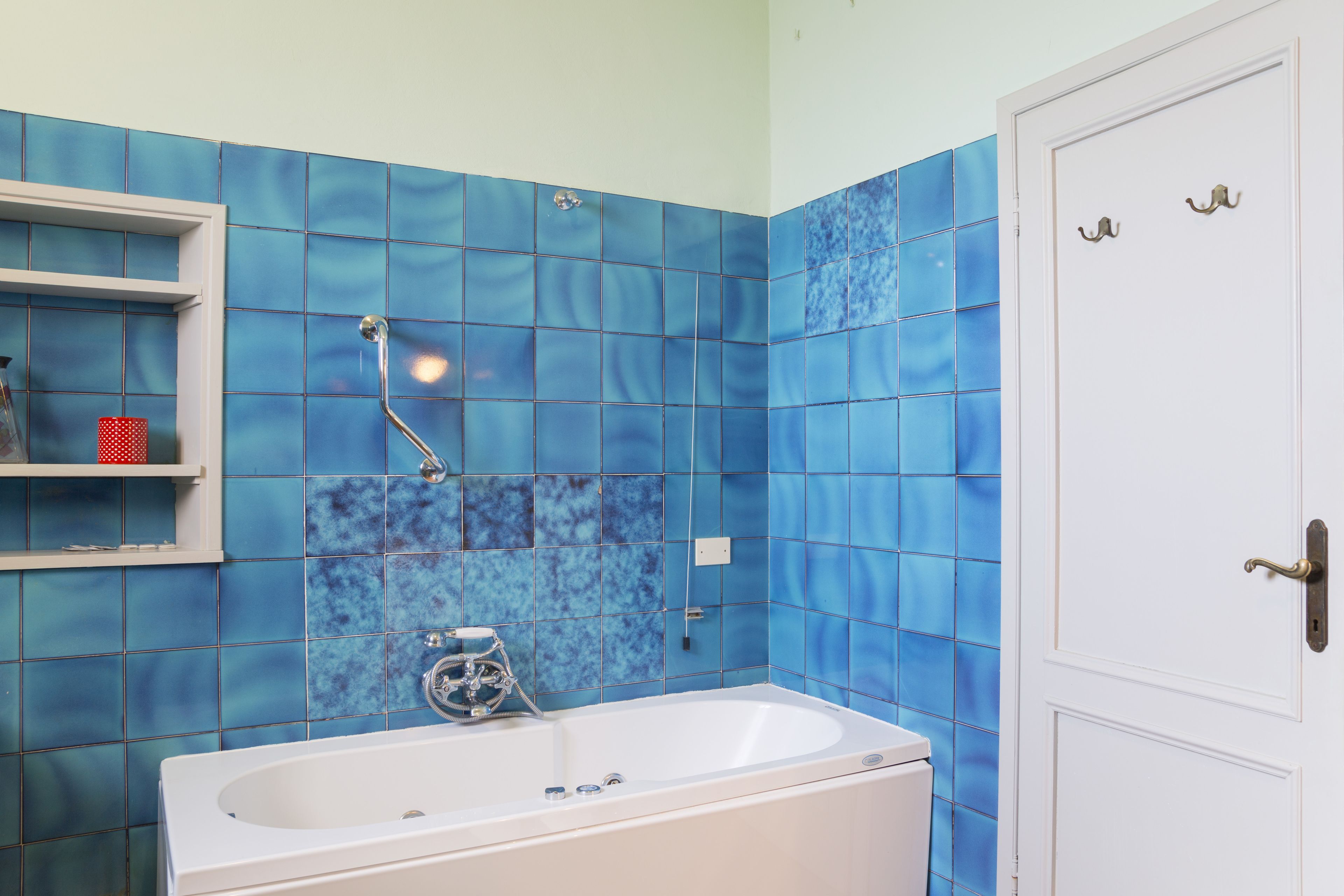 A bathroom with a white bathtub, blue tiled walls, and a white door with two handles.
