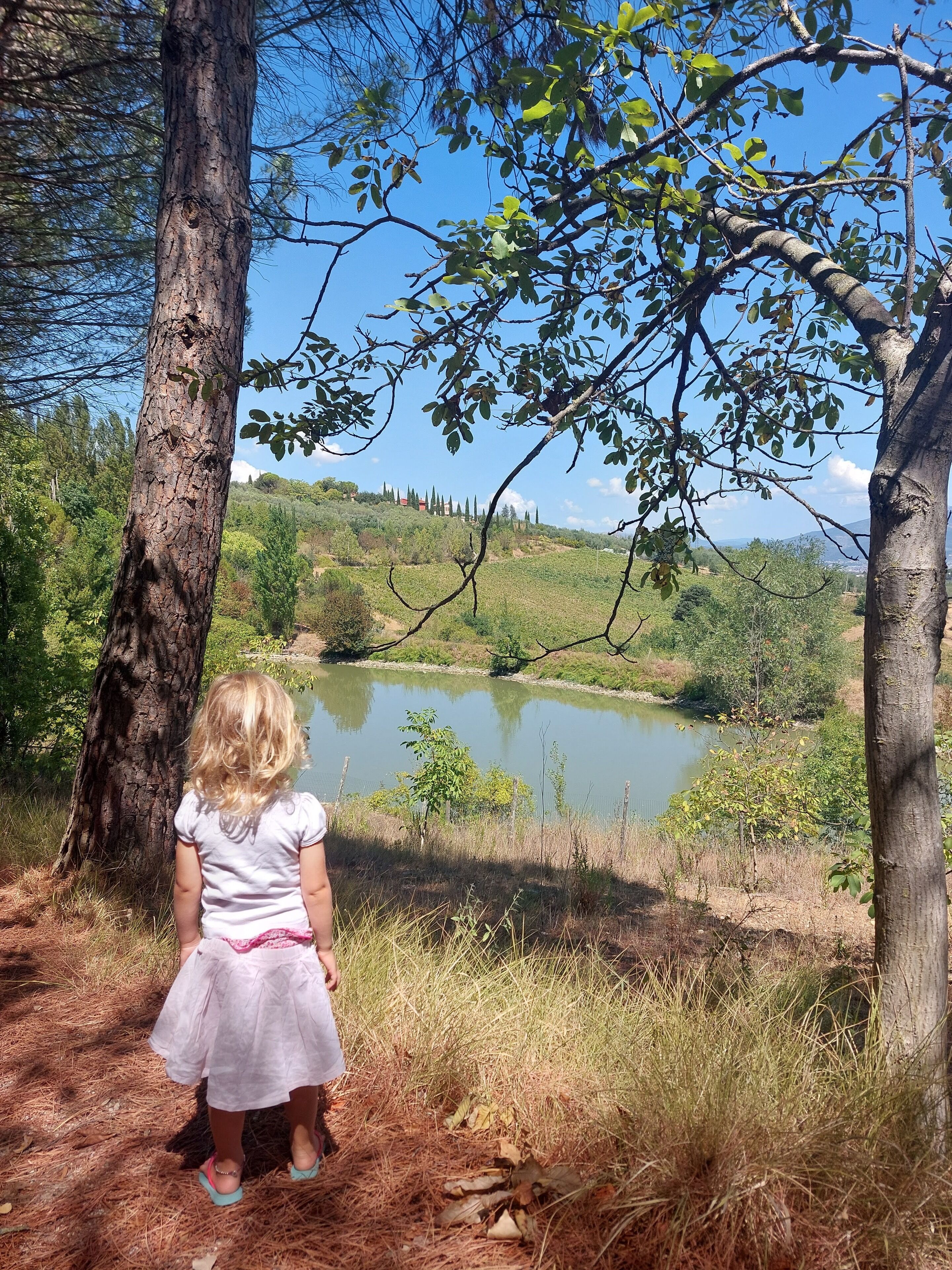 A child standing by a lake with trees and hills in the background.
