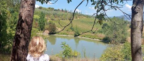 A child standing by a lake with trees and hills in the background.
