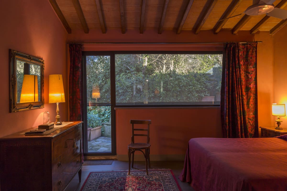 Ein Schlafzimmer mit einem Bett, einem Sessel, einer Kommode, einem Fenster mit Vorhängen und einem Deckenventilator.