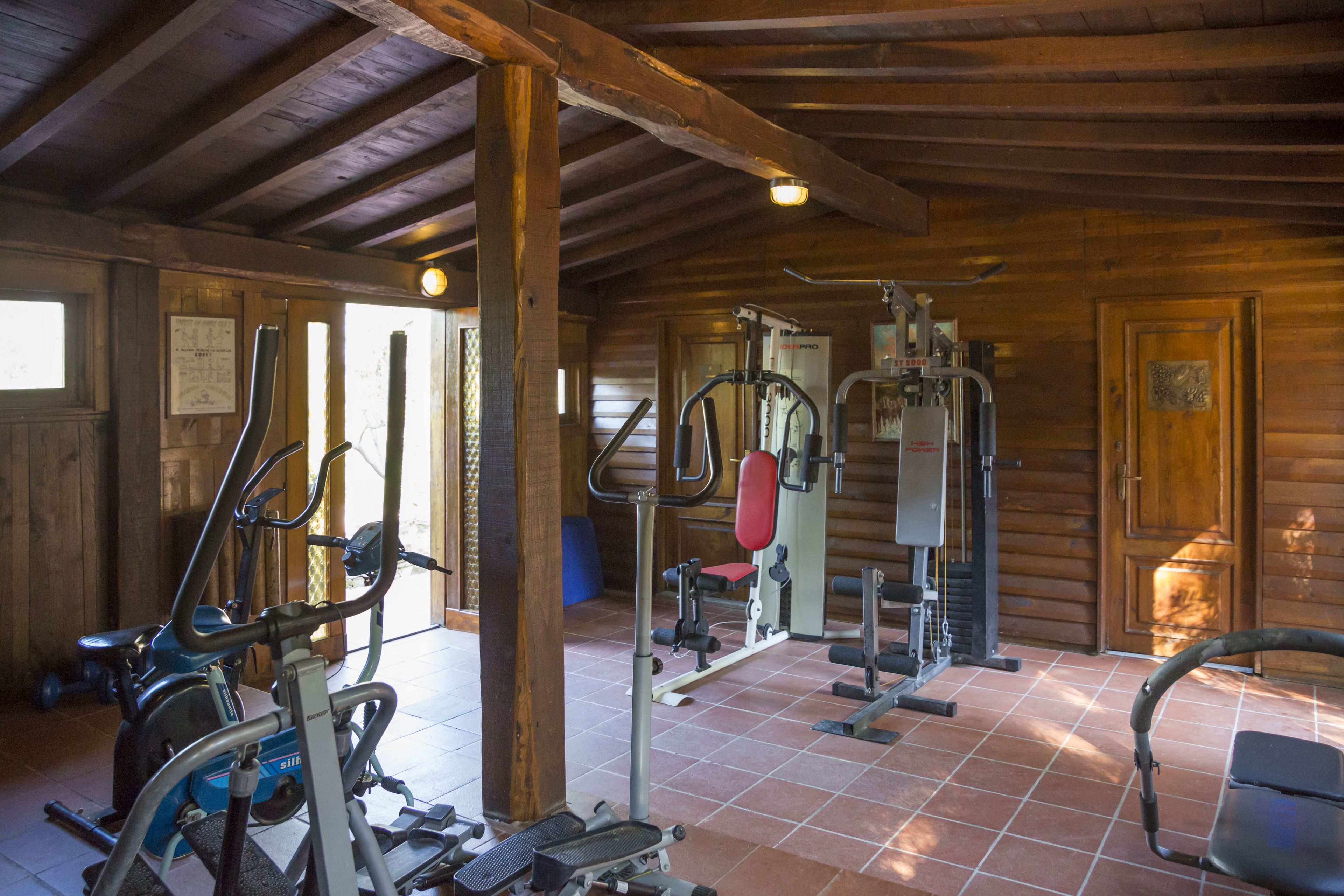 A gym with various exercise equipment, wooden walls, and a tiled floor.