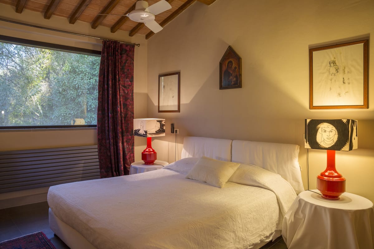 Ein Schlafzimmer mit einem großen Bett, einem Fenster mit Vorhängen, einem Deckenventilator und zwei Nachttischen mit Lampen.