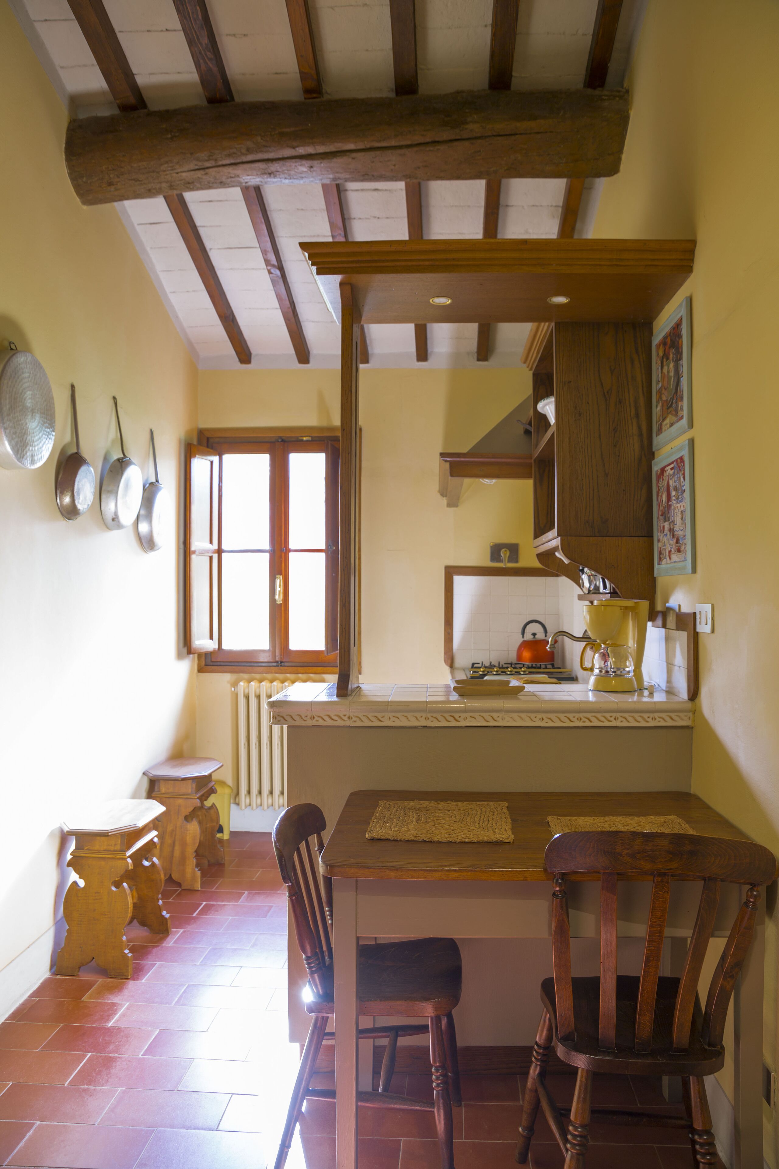 A kitchen with wooden beams, a window, a radiator, and a table with chairs.