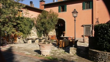 A courtyard with stone flooring, outdoor seating, and a large potted plant.