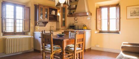 A spacious kitchen with wooden cabinets, a dining table, and chairs. There is a window providing natural light and a radiator under the window.