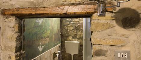 Une salle de bain avec un mur en pierre, un lavabo blanc, un miroir et une fenêtre donnant sur une forêt.