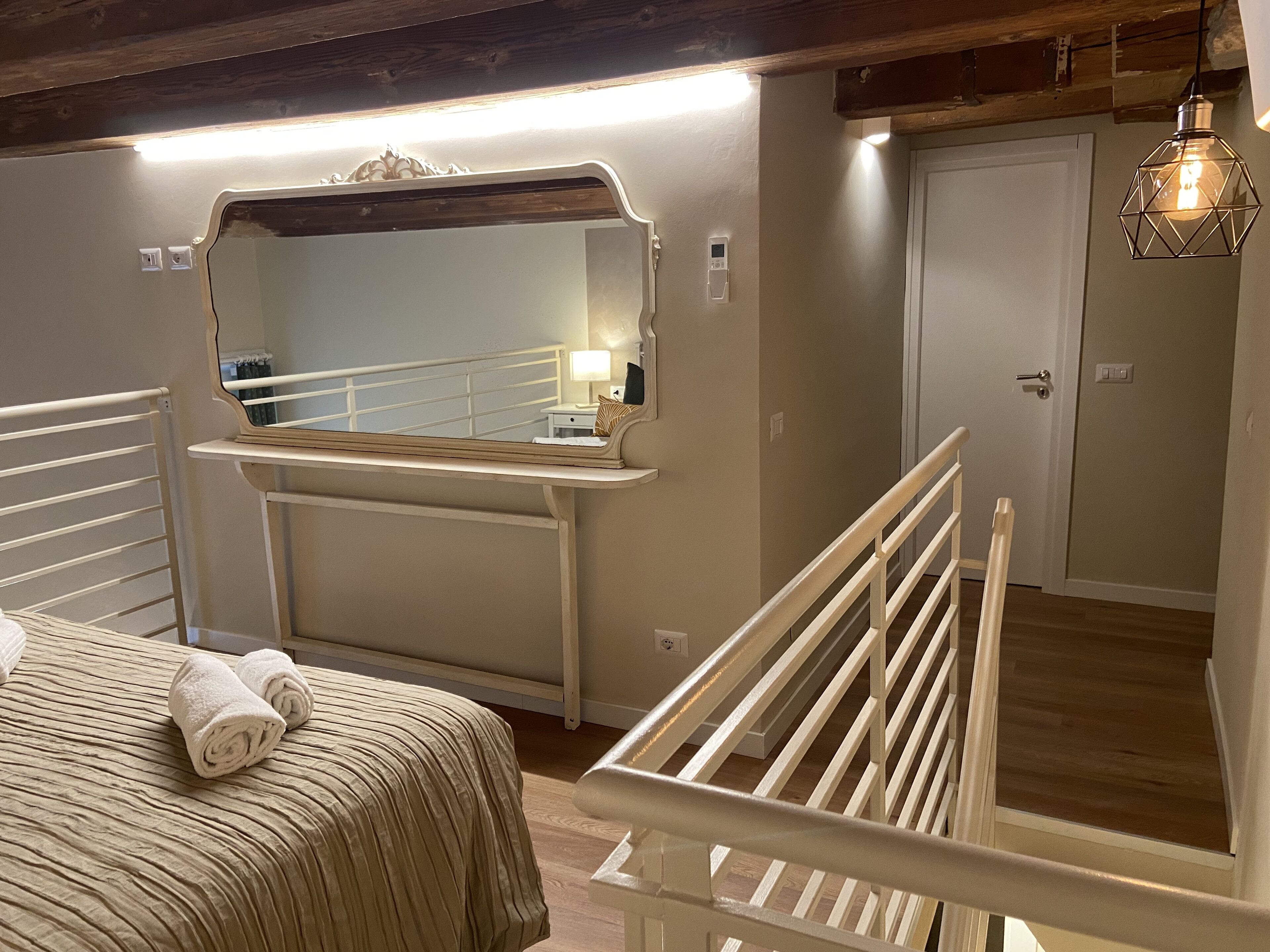 Un dormitorio con cama, mesita de noche, espejo y escalera.