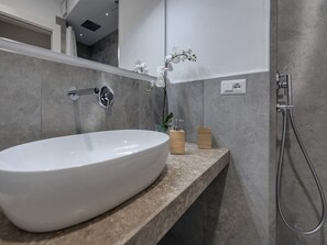 A modern bathroom with a large white sink, a handheld showerhead, and a small orchid plant. - Soggiorno Alessandra (Florence)