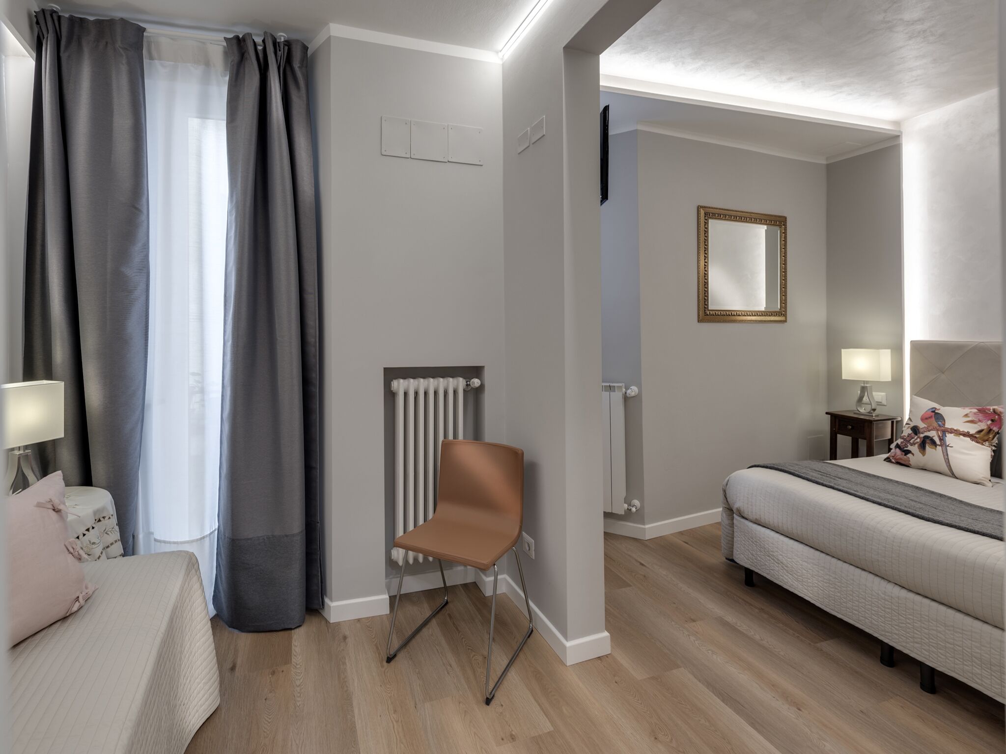 Une chambre d’hôtel moderne, équipée d’un lit, d’une chaise, d’une table de chevet avec une lampe, d’un radiateur et d’un miroir au mur.