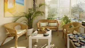 A cozy room with wicker furniture, a white table, and a painting of a beach scene. - Hotel & Studios ASTOR (Antibes)