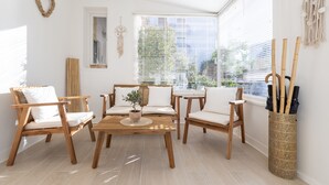 A bright, sunlit room with a wooden table and chairs, a large window with blinds, and a decorative macrame wall hanging. - Hotel & Studios ASTOR (Antibes)