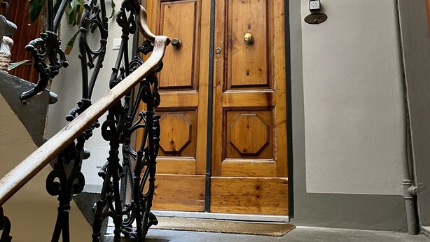 Puerta doble de madera con una celosía metálica, una lámpara arriba y una placa en la pared.