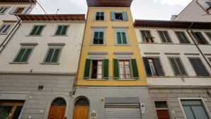 Un edificio de varios pisos con fachada amarilla, persianas verdes y puerta de garaje gris.