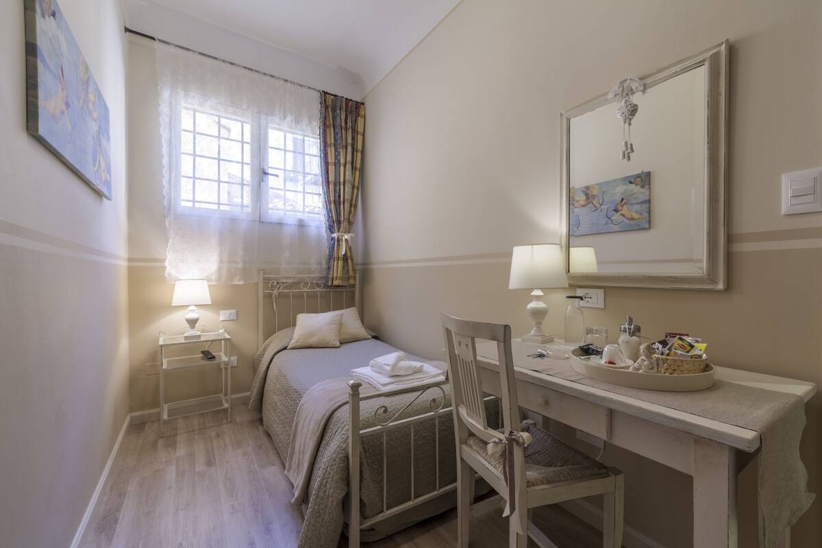 A bedroom with a bed, bedside tables, a desk, a chair, a mirror, and artwork on the walls.